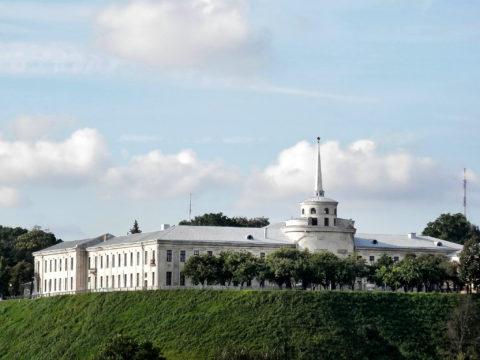 Nowy Zamek w Grodnie. Widok z oddali na zamek i niską wieżę zakończoną w szpic w kształcie obelisku, na szczycie gwiazda