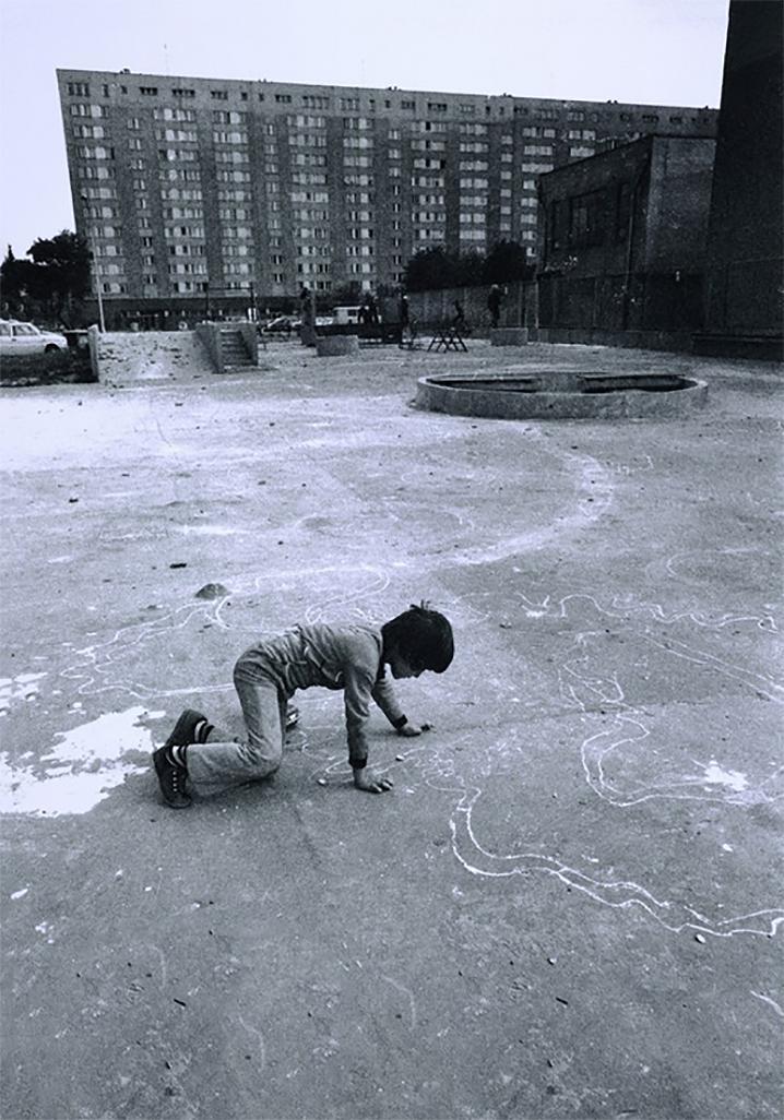 "Betonowa Pustynia" Anna Musiałówna, Cykl Betonowa Pustynia. Osiedle za Żelazną Bramą, lata 70-te, Muzeum Fotografii w Krakowie. Chłopiec rysujący kredą na asfalcie, w tle potężny blok
