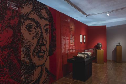 Dokumentacja wystawy poświęconej Mikołajowi Kopernikowi pt. "Misterium Słońca. Kopernik, syn Renesansu". Widok gabloty z księgami, obok rzeźba głowy Kopernika