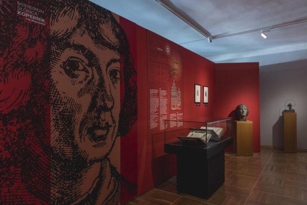 Dokumentacja wystawy poświęconej Mikołajowi Kopernikowi pt. "Misterium Słońca. Kopernik, syn Renesansu". Widok gabloty z księgami, obok rzeźba głowy Kopernika