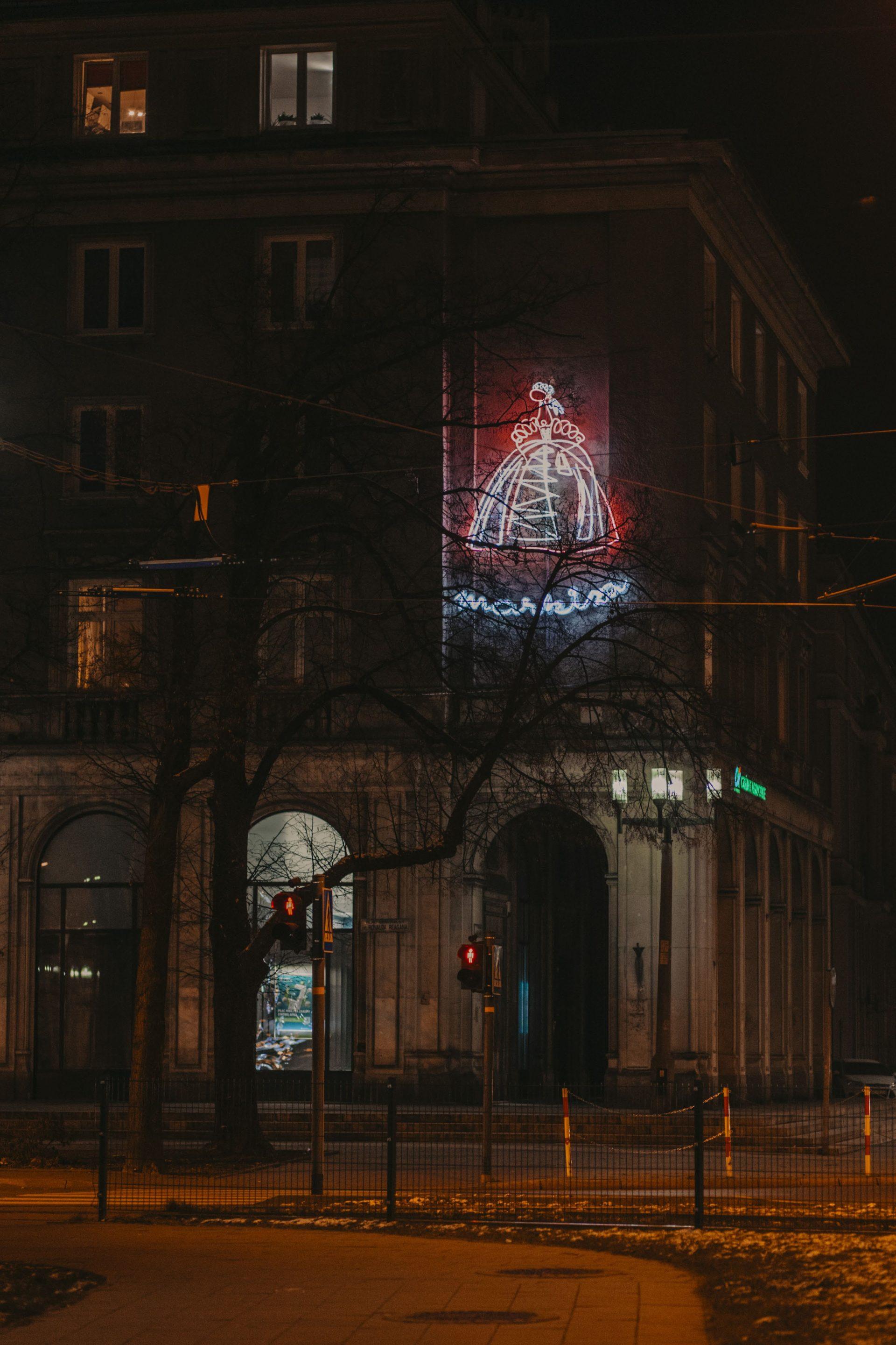 Markiza Widok budynku w nocy zza drzew. Na dole olbrzymie łuki i okna łukowe