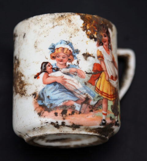 Kubek ceramiczny z malunkiem dziewczynek bawiących się lalką.