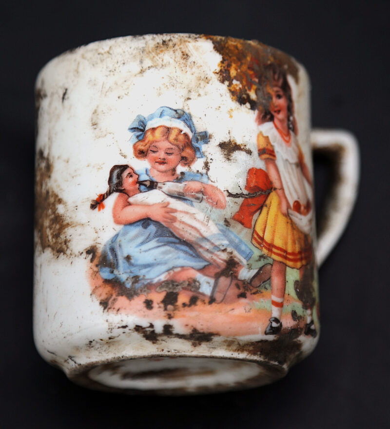 Kubek ceramiczny z malunkiem dziewczynek bawiących się lalką.