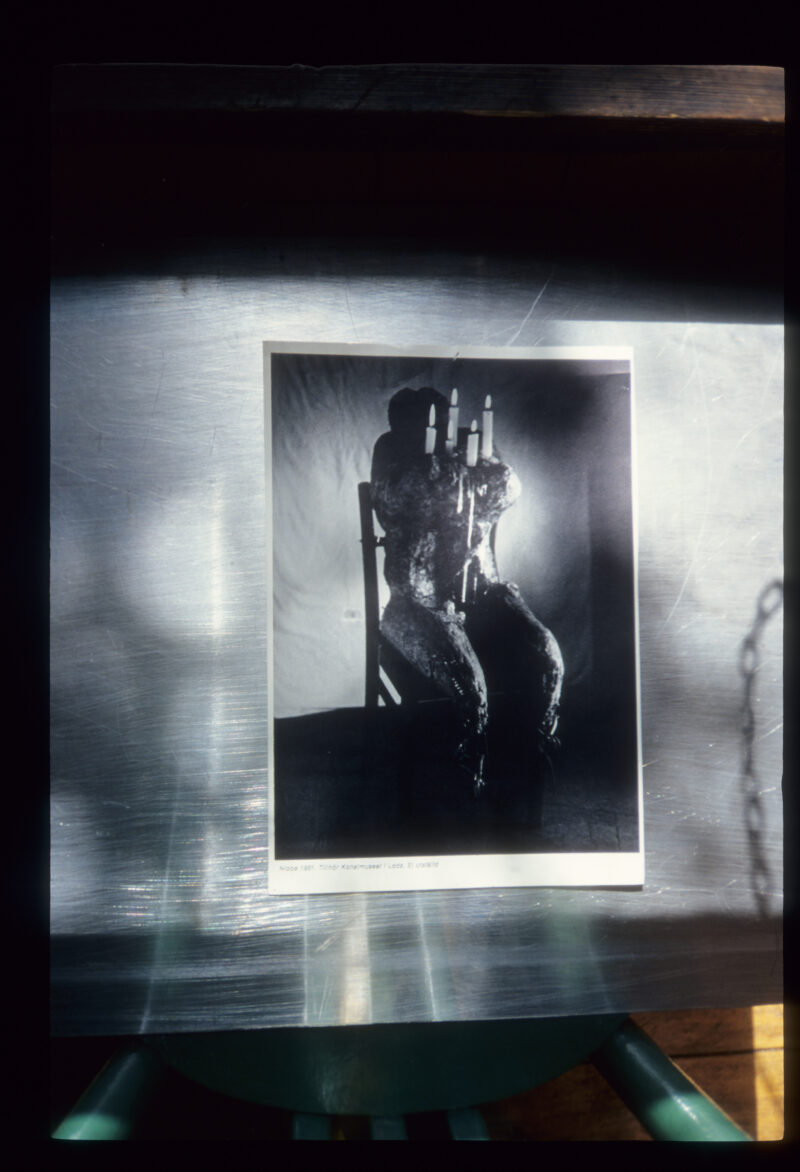 Władysław Hasior, „Notatnik fotograficzny”,z około 1965–1998 roku, z serii „Obiekty”. Na metalowej blasze, fotografia postaci siedzącej, w klatce piersiowej umieszczony ma świecznik.