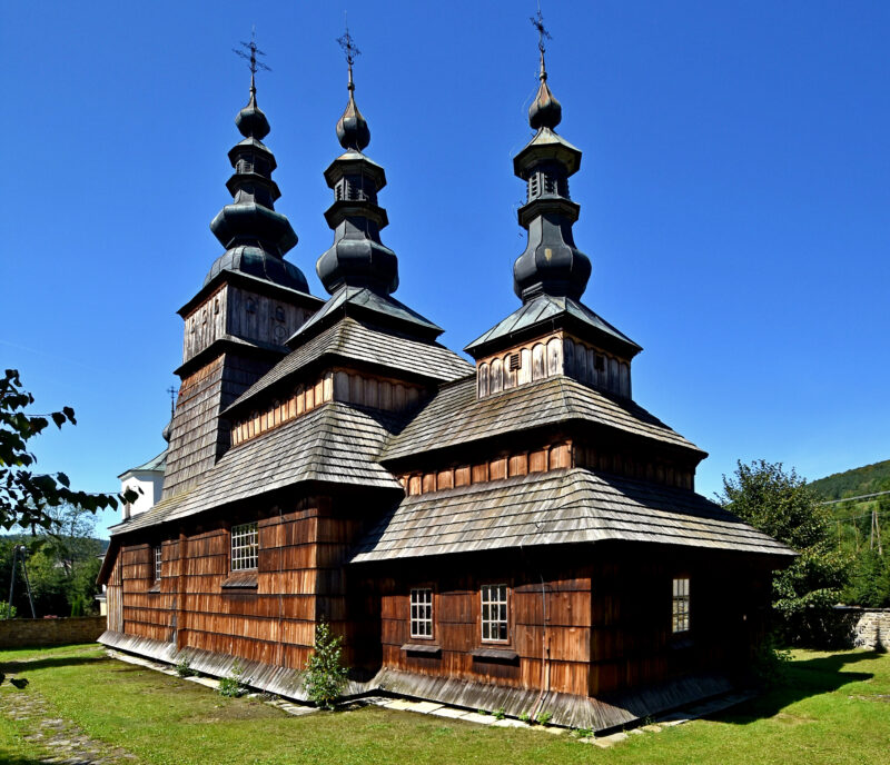 Drewniana cerkiew w Owczarach. Posiada trójczłonowe wieże zwieńczone krzyżami. Od lewej następne wieże schodzą niżej.