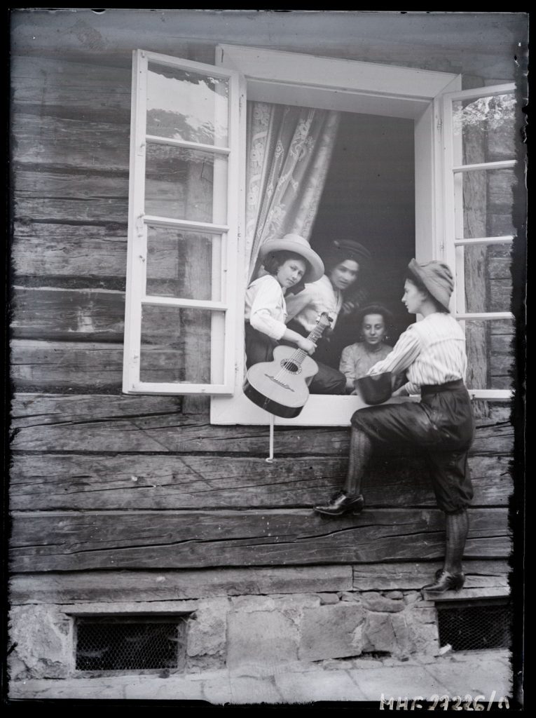 Portret Marii i Klementyny Zubrzyckich (w oknie) oraz Wiktorii podczas inscenizacji występu kobiecej orkiestry . Limanowa, lipiec 1911 r.